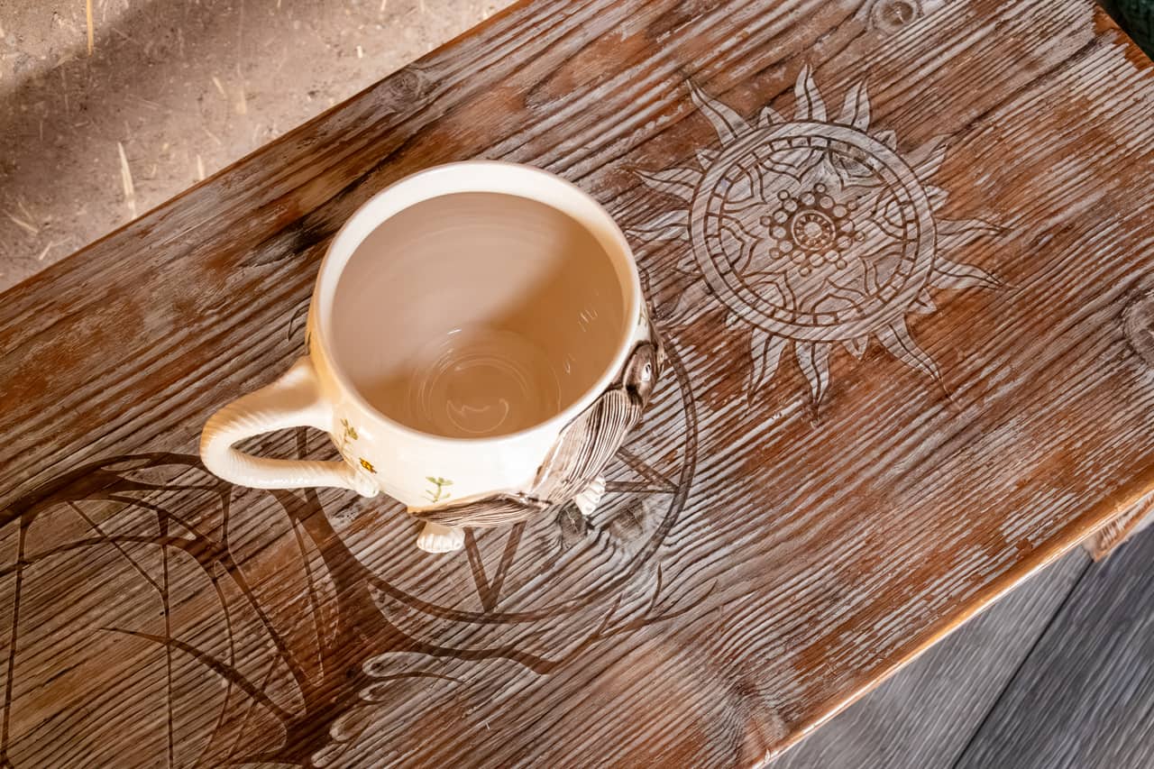 A ceramic cup on a wooden table carved with a sun